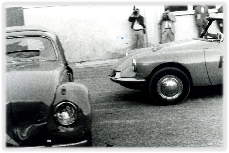Zwei Personen neben einem silbernen Oldtimer auf einer Straße