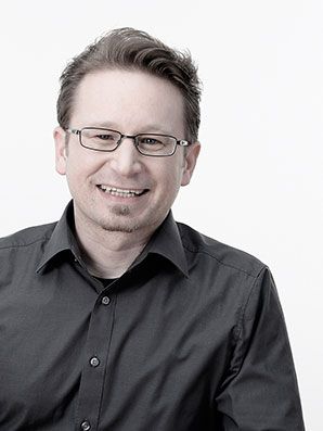 Mann mit Brille und schwarzem Hemd lächelt