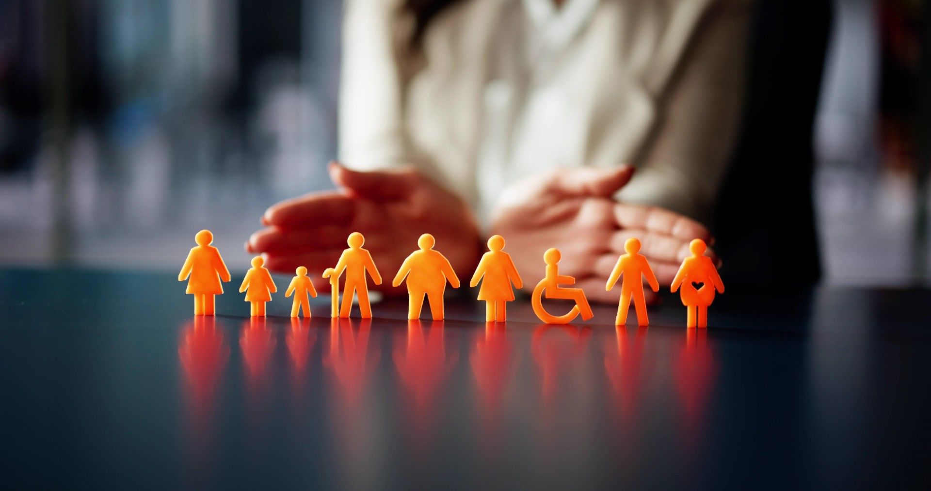 Minifiguren verschiedener Personen, darunter eine Person im Rollstuhl, vor einer Hand