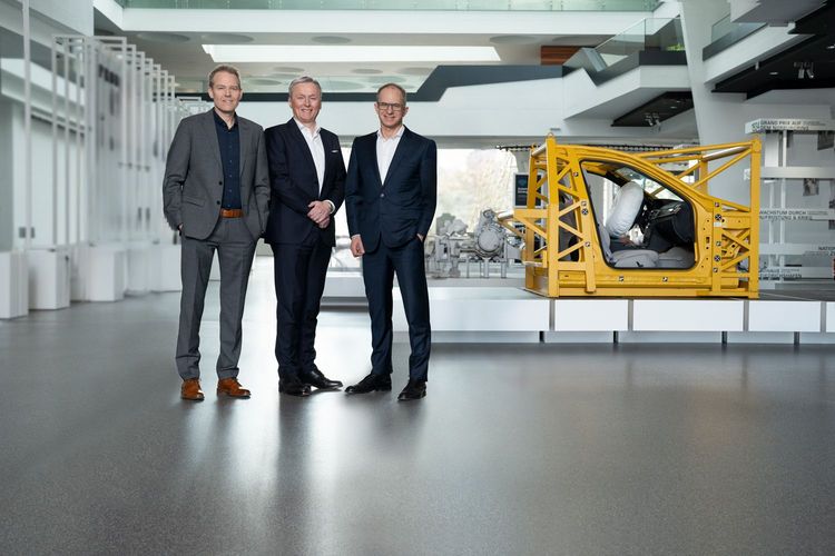 Drei Männer in Anzügen vor einem gelben Fahrzeugsicherheitssystem